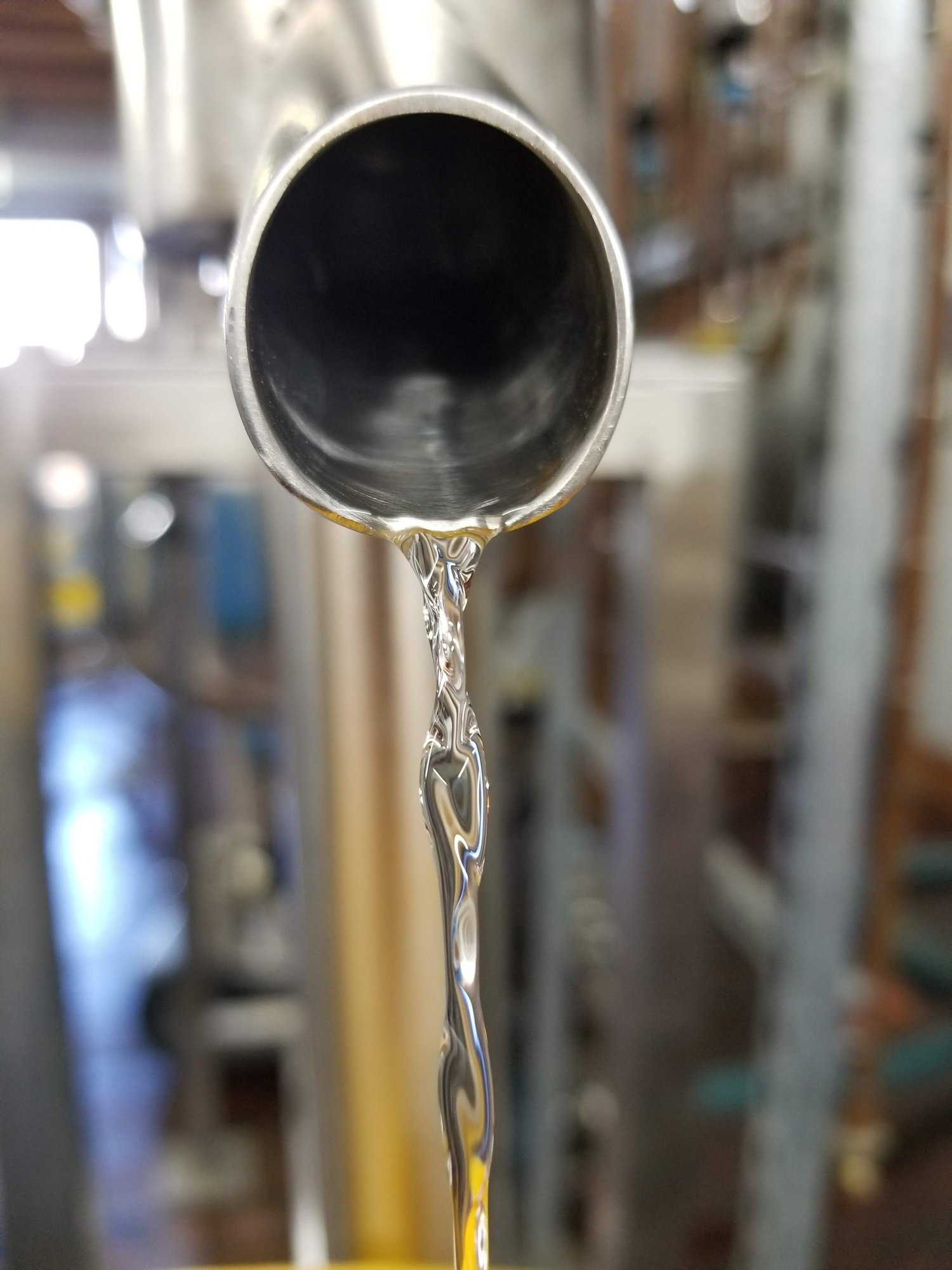 A thin stream of spirit running from a spout on the distillery floor.